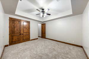 Unfurnished bedroom with carpet flooring, a tray ceiling, and a ceiling fan