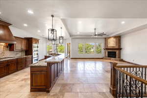 Kitchen with a tiled fireplace, ceiling fan, recessed lighting, a kitchen island with sink, and light stone countertops