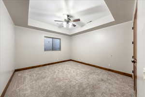 Carpeted spare room with a tray ceiling and ceiling fan