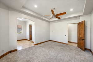 Spare room with a tray ceiling, arched walkways, light colored carpet, ceiling fan, and recessed lighting