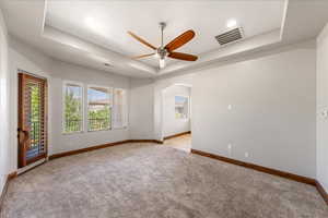Spare room with a tray ceiling, light carpet, arched walkways, ceiling fan, and recessed lighting