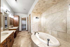 Bathroom featuring two vanities, a jetted tub, and tile walls