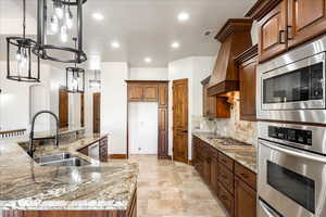 Kitchen with recessed lighting, backsplash, light stone countertops, stainless steel appliances, and custom exhaust hood