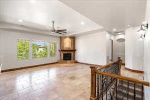 Unfurnished living room with a ceiling fan, recessed lighting, a tiled fireplace, light tile patterned floors, and a raised ceiling
