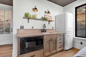 Bar with black microwave, light wood-type flooring, wooden ceiling, and freestanding refrigerator