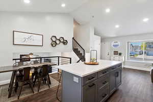 Kitchen with lofted ceiling, dark wood-style flooring, recessed lighting, a center island, and light stone countertops