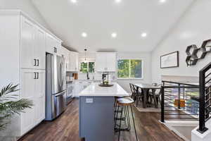 Kitchen featuring lofted ceiling, stainless steel appliances, a breakfast bar area, dark wood-style floors, and tasteful backsplash