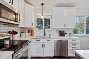 Kitchen featuring appliances with stainless steel finishes, white cabinets, pendant lighting, light stone counters, and decorative backsplash