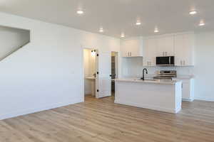 Kitchen featuring appliances with stainless steel finishes, light wood-style flooring, white cabinetry, light countertops, and recessed lighting
