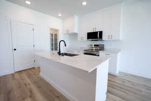 Kitchen featuring appliances with stainless steel finishes, an island with sink, white cabinetry, light wood-type flooring, and recessed lighting