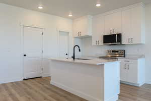 Kitchen featuring appliances with stainless steel finishes, light wood-type flooring, white cabinetry, an island with sink, and recessed lighting