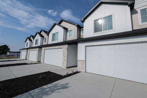 View of side of property featuring concrete driveway, stone siding, an attached garage, board and batten siding, and a residential view
