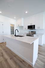 Kitchen featuring appliances with stainless steel finishes, white cabinetry, an island with sink, light wood-style flooring, and recessed lighting