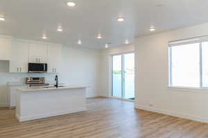 Kitchen featuring appliances with stainless steel finishes, light wood finished floors, light countertops, white cabinets, and a center island with sink