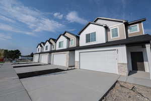View of front of home with concrete driveway, an attached garage, stone siding, and board and batten siding