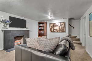 Carpeted living room featuring a textured ceiling, stairway, and a fireplace