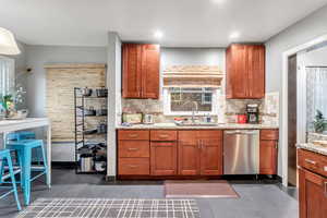 Kitchen with stainless steel dishwasher, tasteful backsplash, light stone countertops, dark tile patterned flooring, and brown cabinets