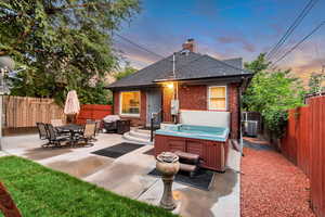 Back of house featuring a hot tub, brick siding, a chimney, a patio area, and a fenced backyard