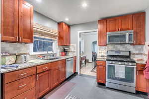 Kitchen with appliances with stainless steel finishes, decorative backsplash, light stone countertops, and recessed lighting