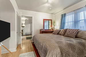 Bedroom featuring crown molding, light wood-style flooring, and arched walkways