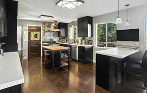 Kitchen with dark cabinets, butcher block counters, dark wood-style flooring, stainless steel appliances, and decorative light fixtures