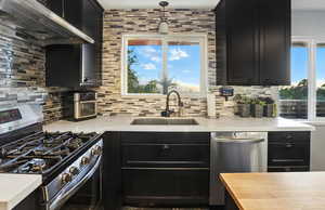 Kitchen featuring appliances with stainless steel finishes, dark cabinets, exhaust hood, and backsplash