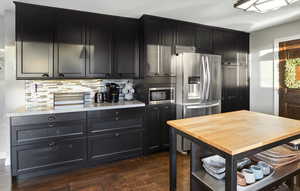 Kitchen featuring dark cabinets, dark wood-style floors, stainless steel appliances, light countertops, and backsplash