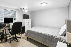 Carpeted bedroom featuring a textured ceiling and a desk