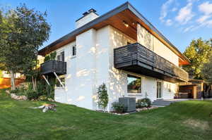 Rear view of house featuring a balcony, a yard, and brick siding