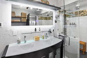 Full bathroom featuring a textured wall, double vanity, and a shower stall