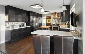 Kitchen with decorative backsplash, light countertops, dark cabinetry, and stainless steel appliances