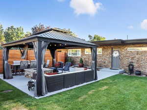 Back of property featuring outdoor lounge area, a gazebo, a lawn, a patio area, and brick siding