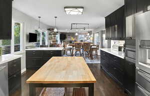 Kitchen featuring dark wood-style floors, dark cabinetry, appliances with stainless steel finishes, open floor plan, and hanging light fixtures