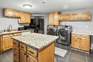 Kitchen featuring separate washer and dryer, a kitchen island, a textured ceiling, black fridge with ice dispenser, and dark tile patterned floors