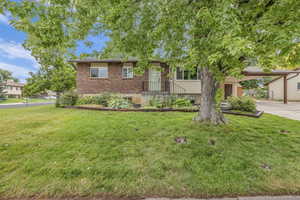 View of front facade featuring brick siding, an attached carport, a front lawn, and concrete driveway