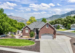 View of front of property with brick siding, concrete driveway, a front yard, a mountain view, and a storage shed