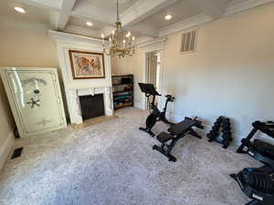 Workout area featuring coffered ceiling, a chandelier, crown molding, a fireplace with flush hearth, and recessed lighting