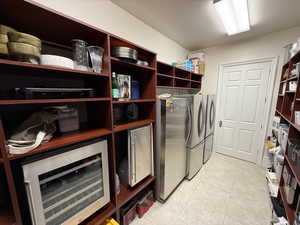 Washroom with beverage cooler, independent washer and dryer, and light tile patterned flooring