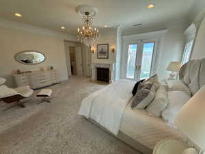 Bedroom with ornamental molding, access to exterior, carpet flooring, a chandelier, and a fireplace with flush hearth