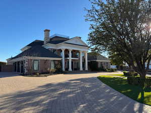 View of front of property with decorative driveway, a balcony, a chimney, brick siding, and a garage