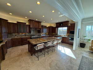 Kitchen featuring tasteful backsplash, a kitchen breakfast bar, a large island, dark stone countertops, and ornamental molding