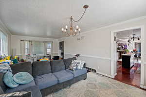 Living room with a textured ceiling, healthy amount of natural light, a chandelier, crown molding, and wood finished floors