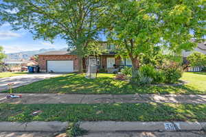 Obstructed view of property featuring an attached garage, brick siding, concrete driveway, and a front yard