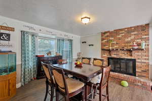 Dining area featuring wood finished floors, crown molding, a brick fireplace, and a textured ceiling