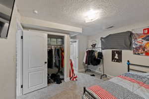 Carpeted bedroom featuring a textured ceiling and a closet
