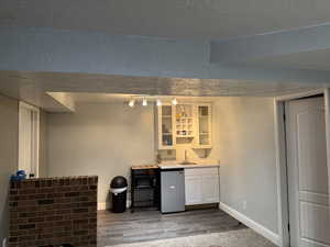 Indoor wet bar featuring a textured wall, a textured ceiling, light wood-style floors, and fridge