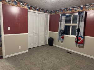 Unfurnished bedroom with a textured ceiling, carpet floors, and a closet