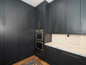 Kitchen with stainless steel double oven, light wood-type flooring, light stone counters, and dark cabinetry