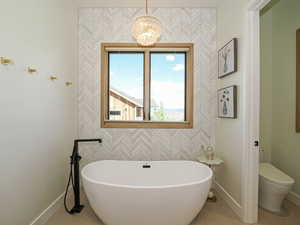 Full bathroom with a freestanding tub, a chandelier, and wallpapered walls