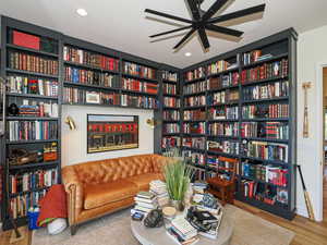 Sitting room featuring wall of books, wood finished floors, a ceiling fan, and recessed lighting